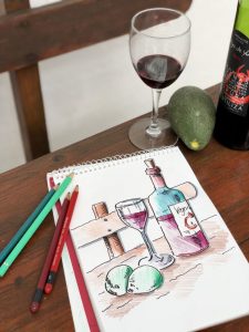 Skizzenbuch mit einem gezeichneten Bild welches Weinglas, Weinflasche und zwei Avocados zeigt.