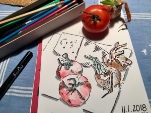 Ein Skizzenbuch mit einem gezeichneten Tomatenstillleben. Daneben eine reale Tomate als Vorlage.